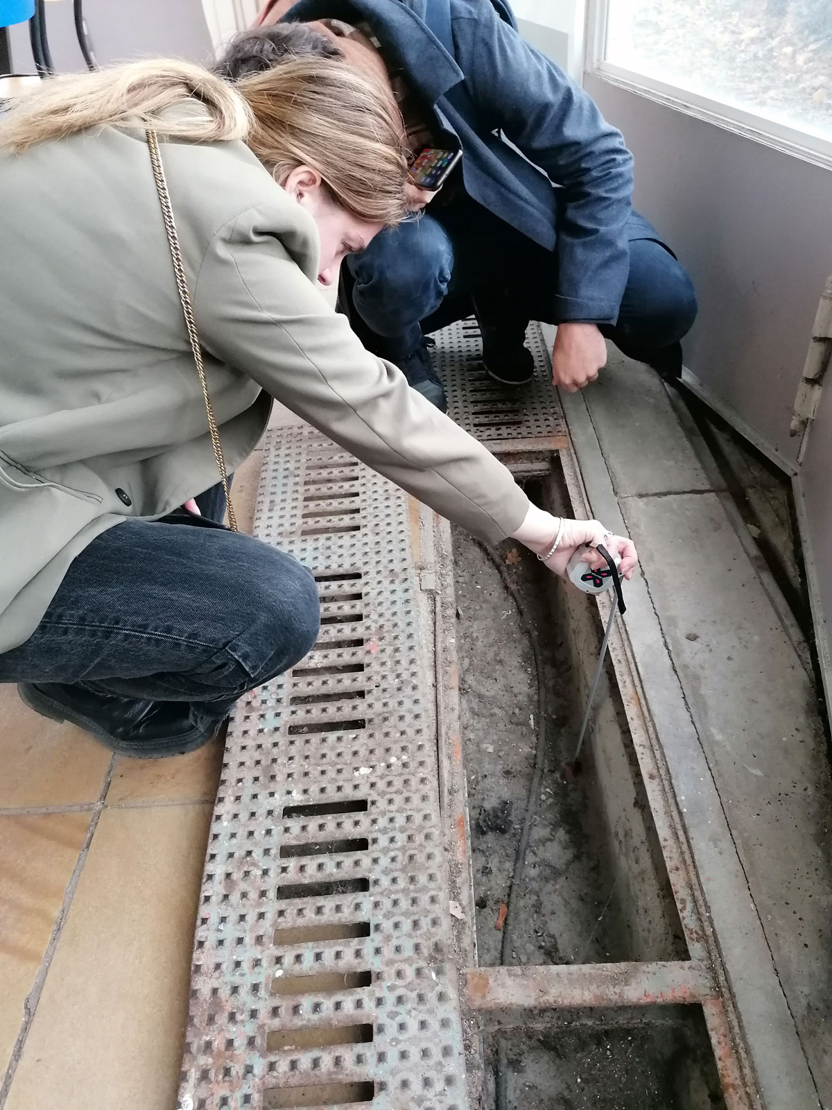Deux personnes accroupies mesurent la hauteur d'un caniveau en bordure d'une fenêtre d'un pavillon de l'école de plein air.